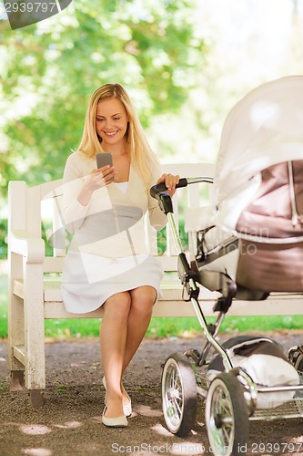 Image of happy mother with smartphone and stroller in park