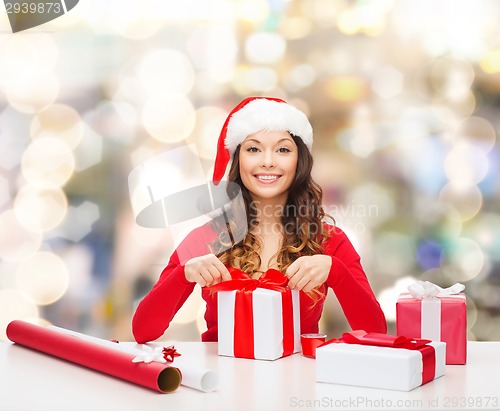 Image of smiling woman in santa helper hat packing gifts