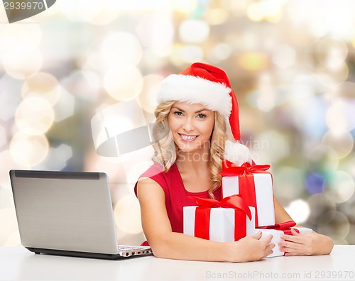 Image of smiling woman in santa hat with gifts and laptop