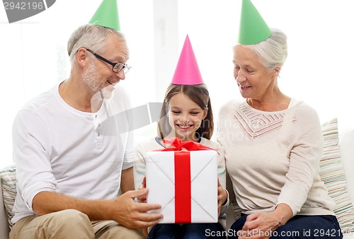 Image of smiling family in party hats with gift box at home