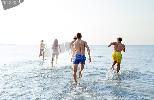 Image of smiling friends running on beach from back