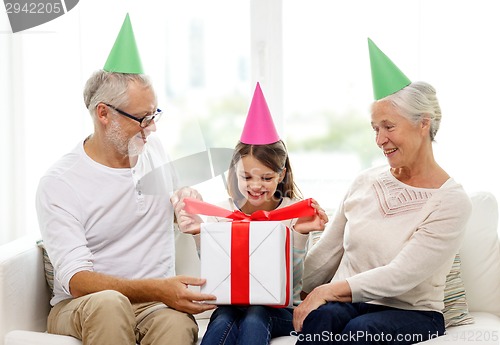Image of smiling family in party hats with gift box at home