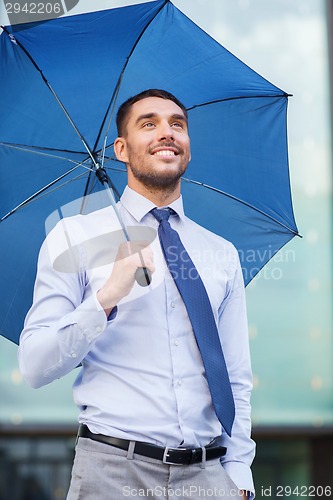 Image of young smiling businessman with umbrella outdoors