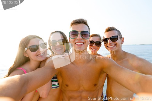 Image of group of smiling friends making selfie on beach