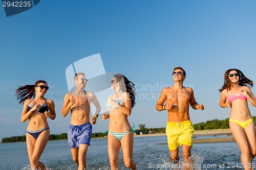 Image of smiling friends in sunglasses running on beach