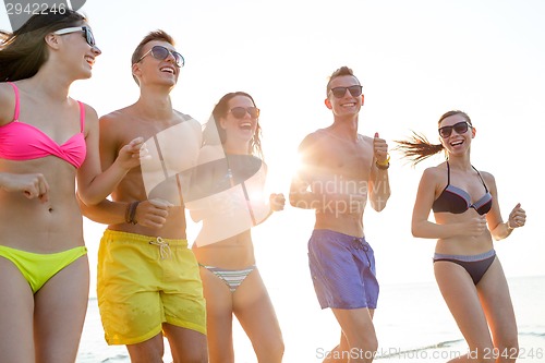 Image of smiling friends in sunglasses running on beach