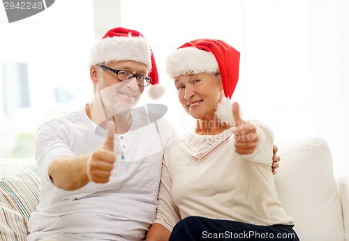 Image of happy senior couple in santa helper hats at home