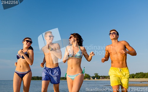 Image of smiling friends in sunglasses running on beach