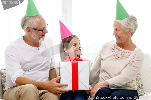 Image of smiling family in party hats with gift box at home