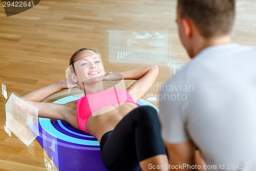 Image of smiling woman with male trainer exercising in gym