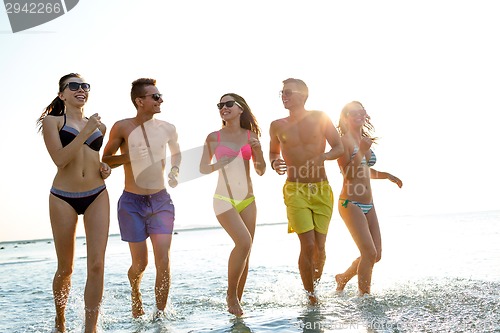 Image of smiling friends in sunglasses running on beach