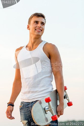 Image of smiling teenage boy with skateboard outdoors