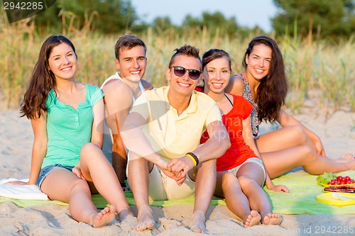 Image of smiling friends sitting on summer beach