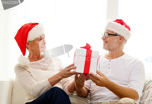 Image of happy senior couple in santa hats with gift box