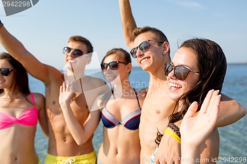 Image of smiling friends in sunglasses on summer beach