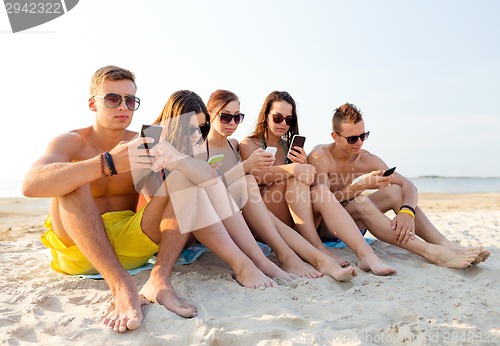 Image of group of friends with smartphones on beach