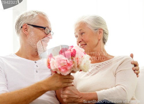 Image of happy senior couple with bunch of flowers at home