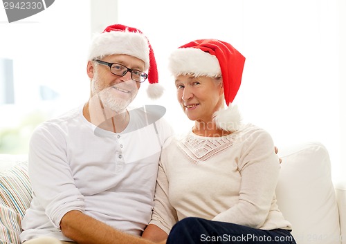 Image of happy senior couple in santa helper hats at home
