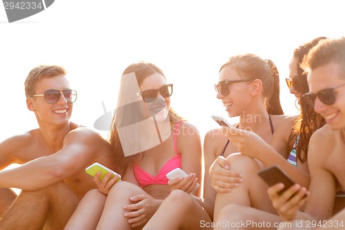 Image of group of smiling friends with smartphones on beach