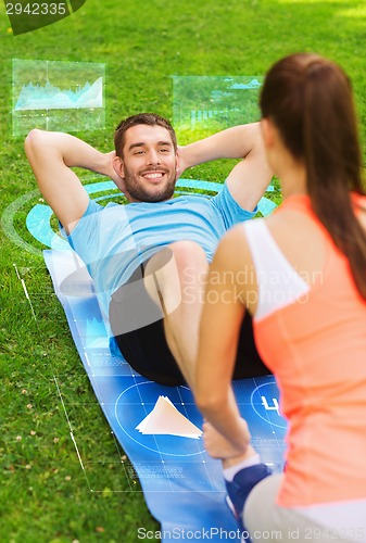 Image of smiling couple doing exercises on mat outdoors