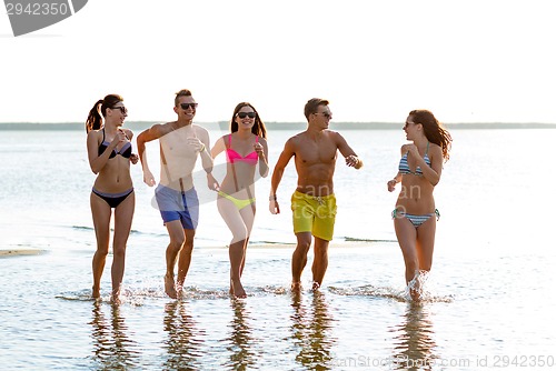 Image of smiling friends in sunglasses running on beach