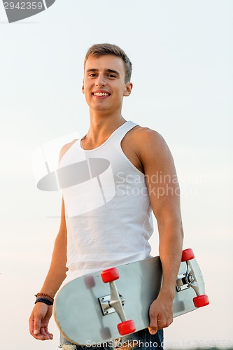 Image of smiling teenage boy with skateboard outdoors