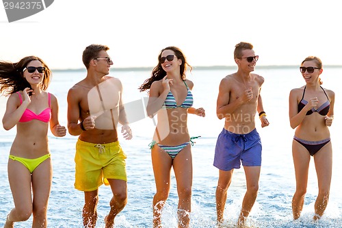 Image of smiling friends in sunglasses running on beach