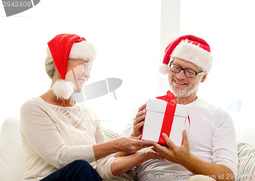 Image of happy senior couple in santa hats with gift box