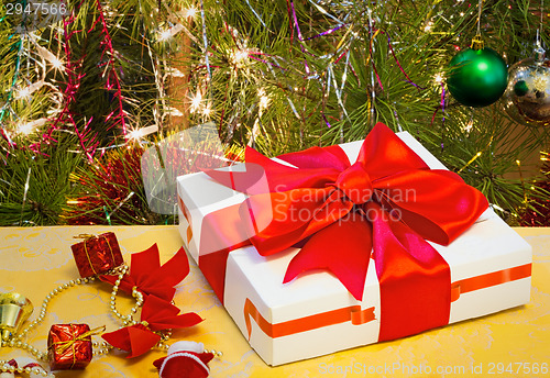 Image of Beautifully packed gift by Christmas and the decorated fir-tree.