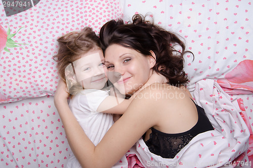 Image of Mum embraces daughter lying in bed