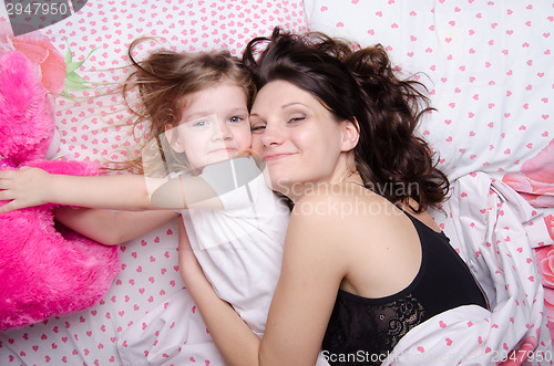 Image of Daughter reaches for a soft toy lying with her mother