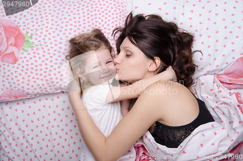 Image of Mum kisses the daughter lying in bed