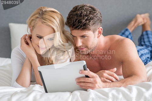 Image of Sweet Couple on Bed Watching Something in Tablet