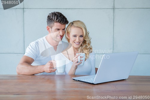 Image of Couple drinking coffee and reading on a laptop