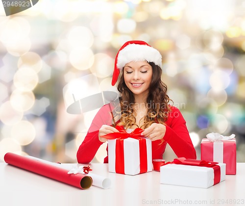 Image of smiling woman in santa helper hat packing gifts