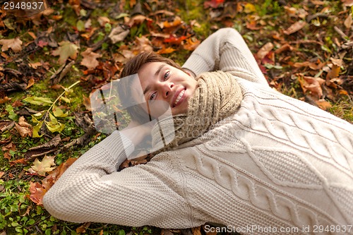 Image of close up of smiling young man lying in autumn park