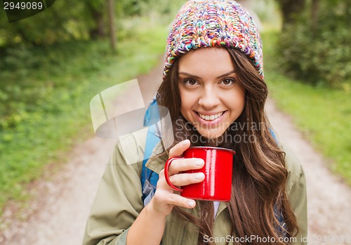 Image of smiling young woman with cup and backpack hiking