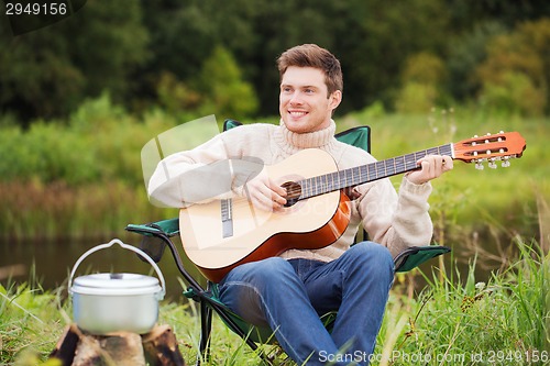 Image of smiling man with guitar and dixie in camping