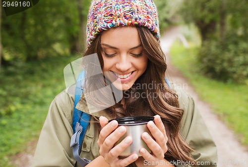 Image of smiling young woman with cup and backpack hiking