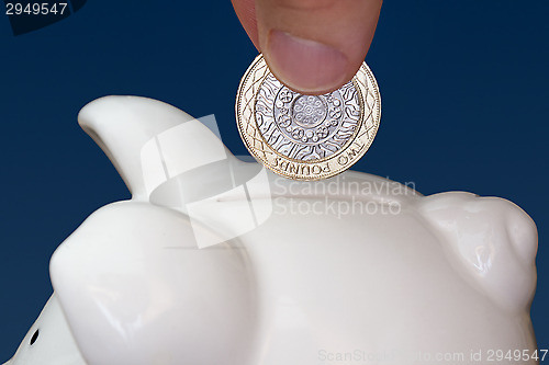 Image of Male hand putting a coin into piggy bank 