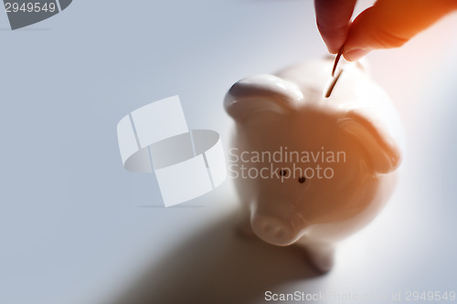 Image of Male hand putting a coin into piggy bank 