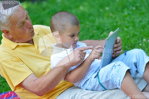 Image of grandfather and child in park using tablet