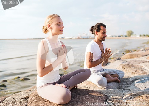 Image of smiling couple making yoga exercises outdoors
