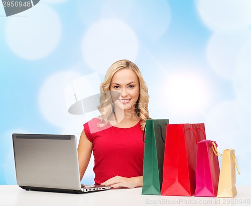 Image of smiling woman in red dress with gifts and laptop