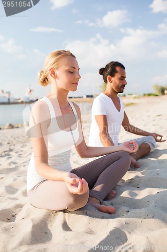 Image of smiling couple making yoga exercises outdoors