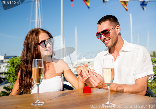 Image of smiling couple with champagne and gift at cafe