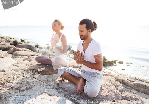 Image of smiling couple making yoga exercises outdoors