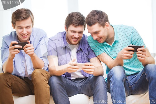 Image of smiling friends with smartphones at home