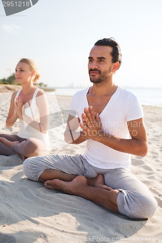 Image of smiling couple making yoga exercises outdoors