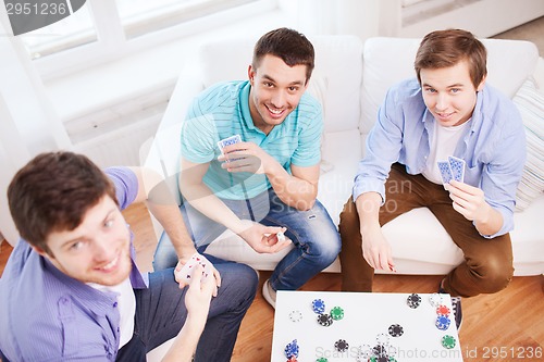 Image of three smiling male friends playing cards at home